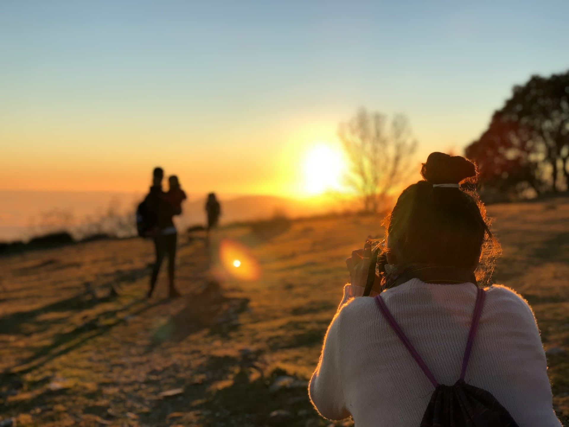 Someone taking a photo at sunset on a hilltop, silhouettes ahead of them