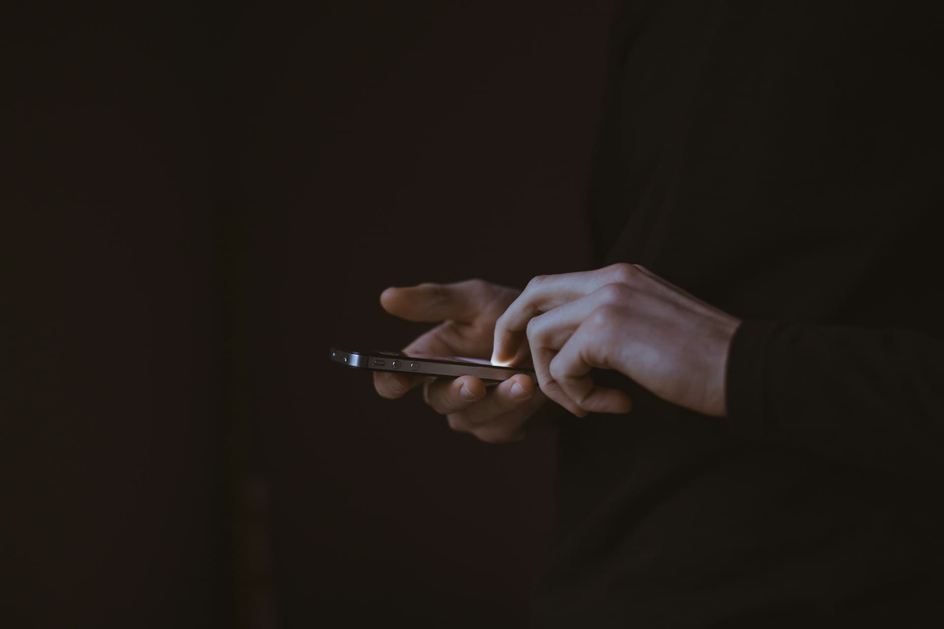 Hands using a phone in low light, screen glow on the fingertips